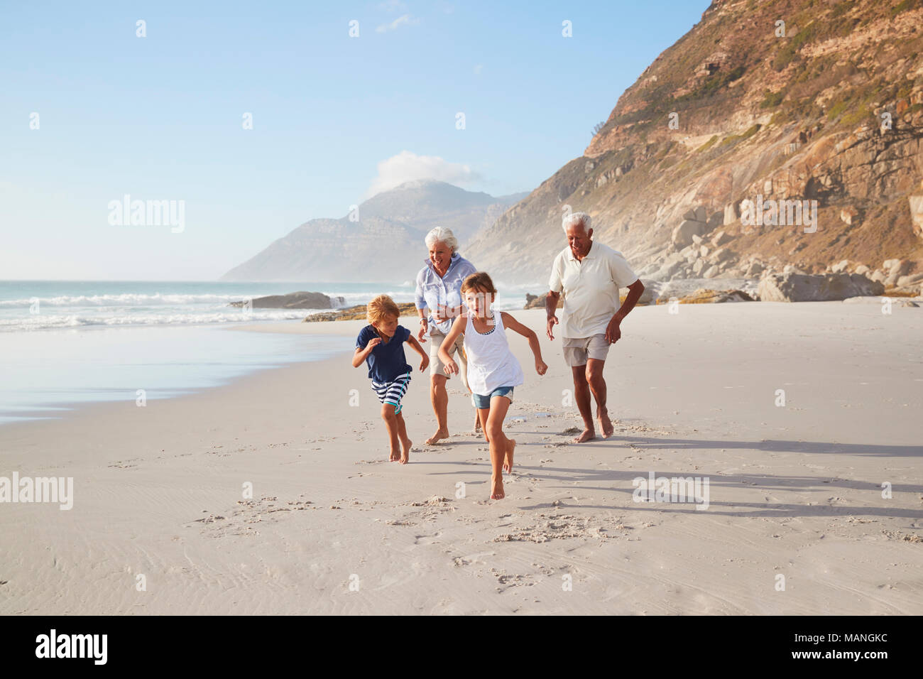 Grandparents Running Along Beach With Grandchildren On Summer Vacation Stock Photo