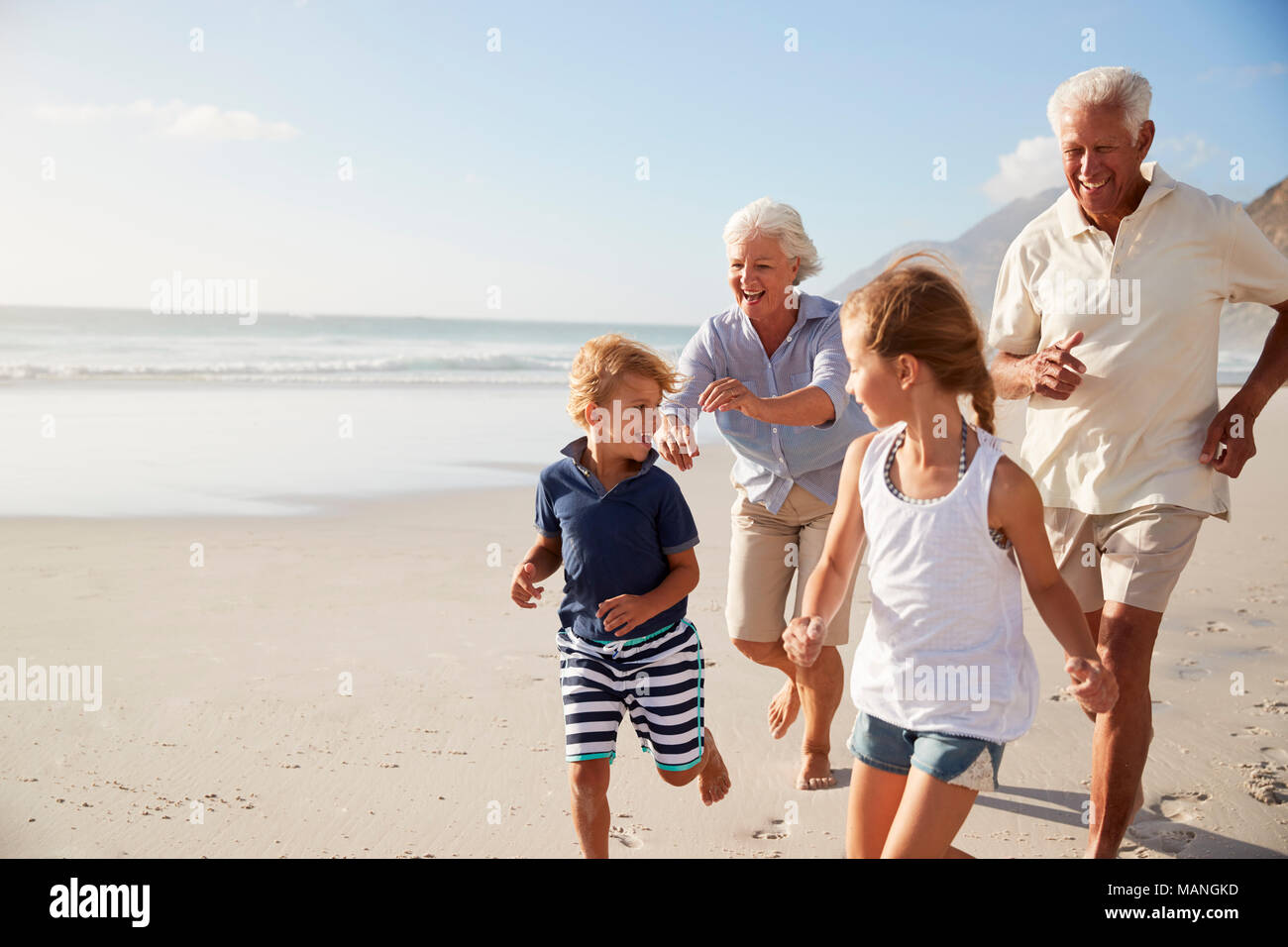 Grandparents Running Along Beach With Grandchildren On Summer Vacation Stock Photo