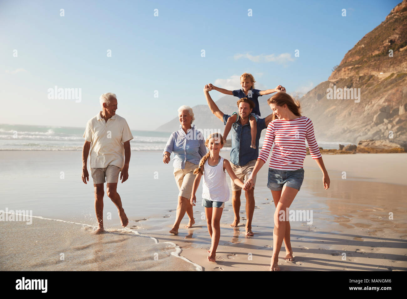 Multi Generation Family On Vacation Walking Along Beach Together Stock Photo