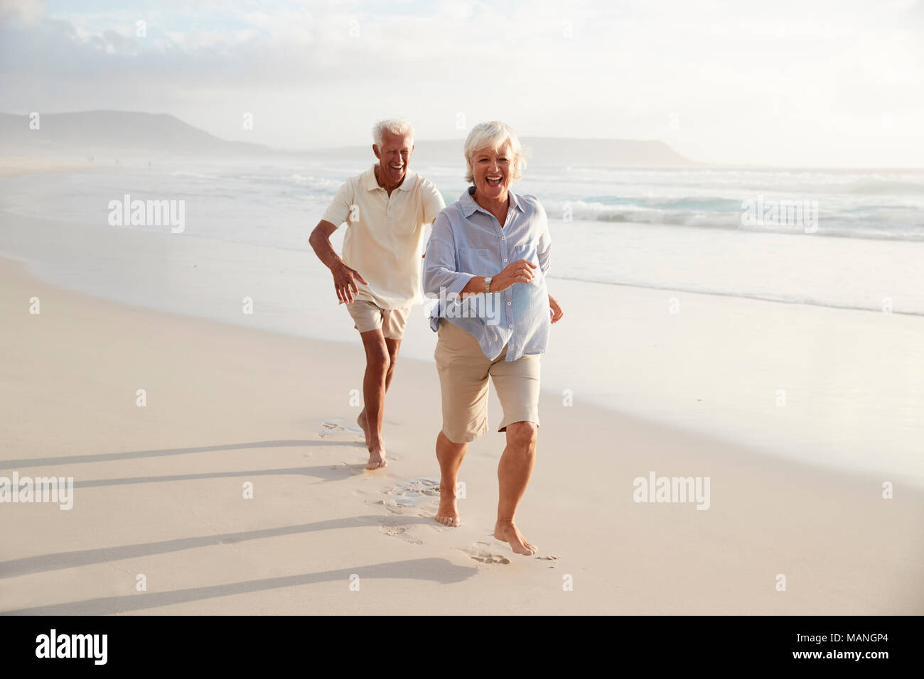 Senior Retired Couple Running Along Summer Beach Together Stock Photo
