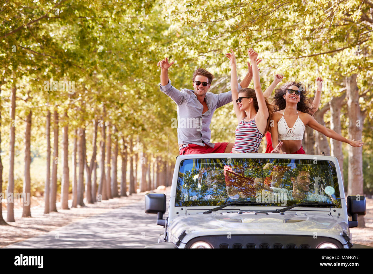 Friends stand waving from the back of an open top car Stock Photo