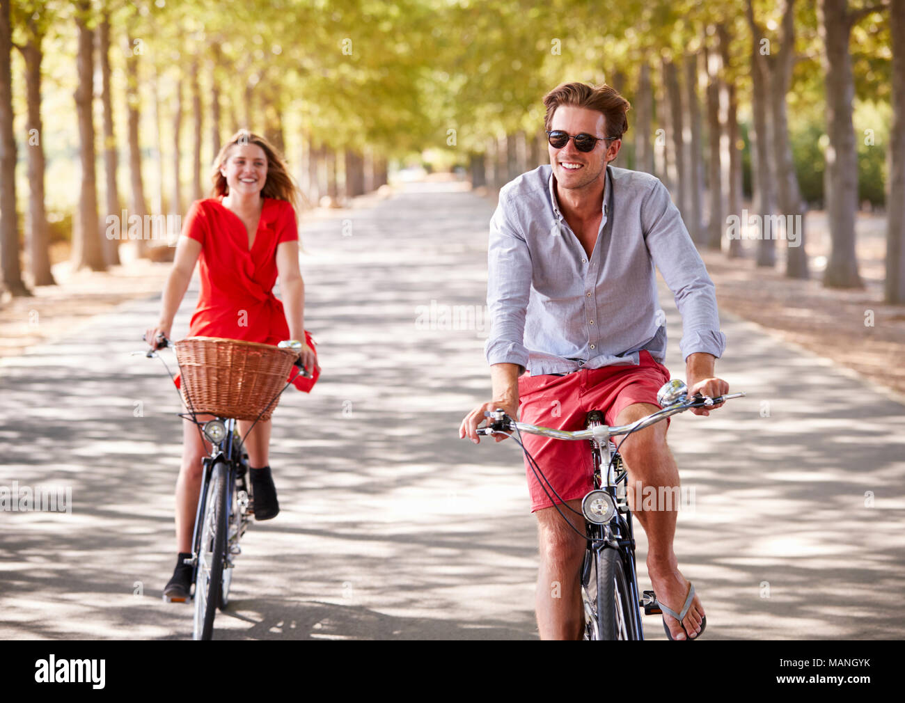 Young white adult couple riding bikes on a tree lined road Stock Photo
