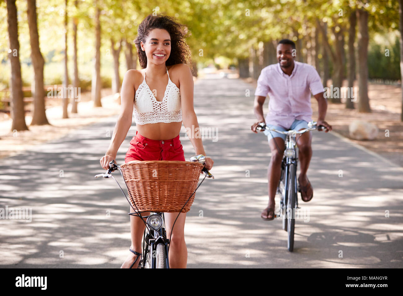 Young mixed race couple riding bicycles on a tree lined road Stock Photo