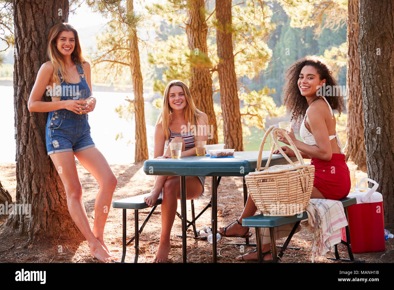 Three female friends hanging out by a lake smiling to camera Stock Photo