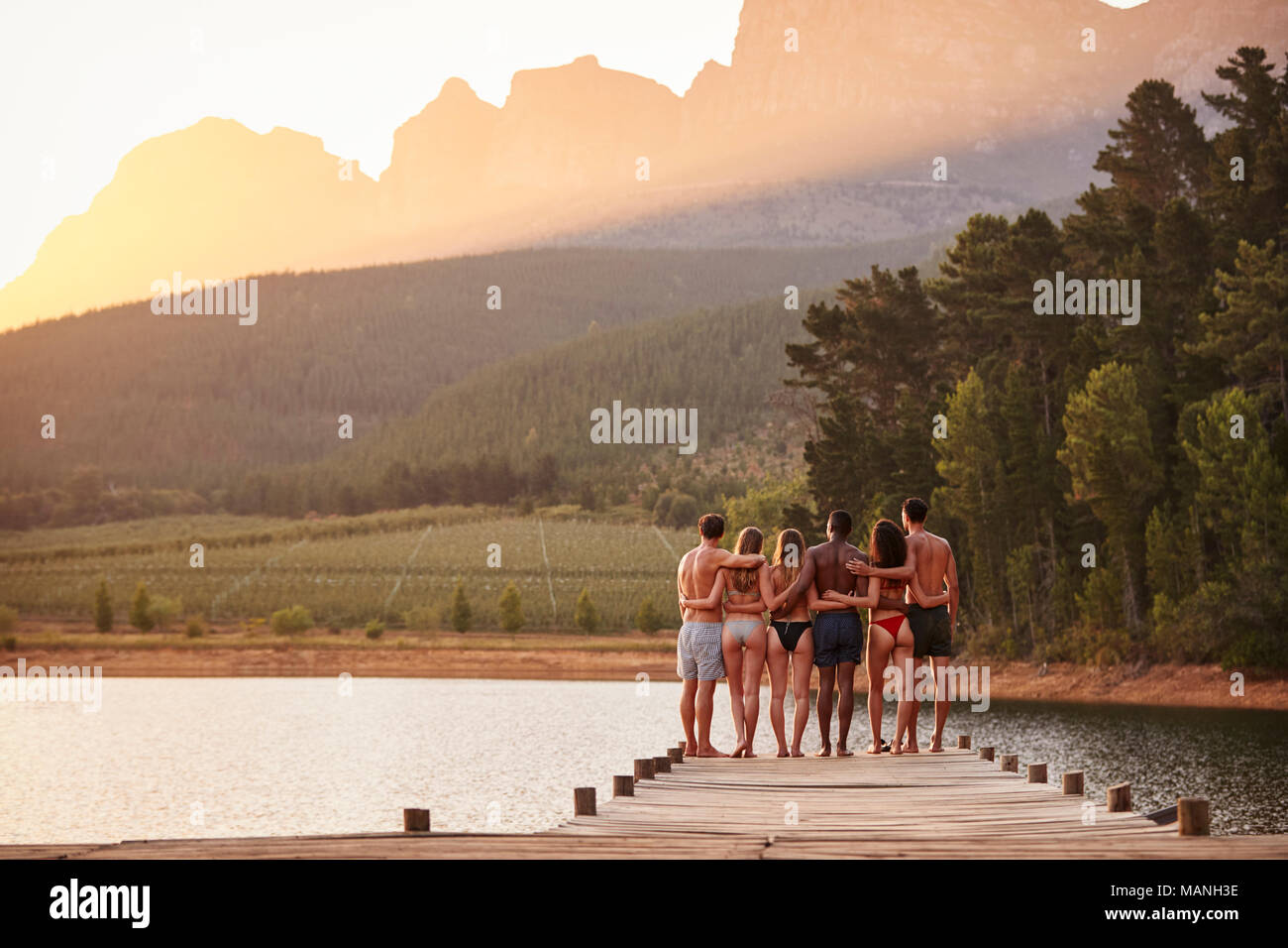 young adult friends standing on a jetty in a lake, back view Stock Photo