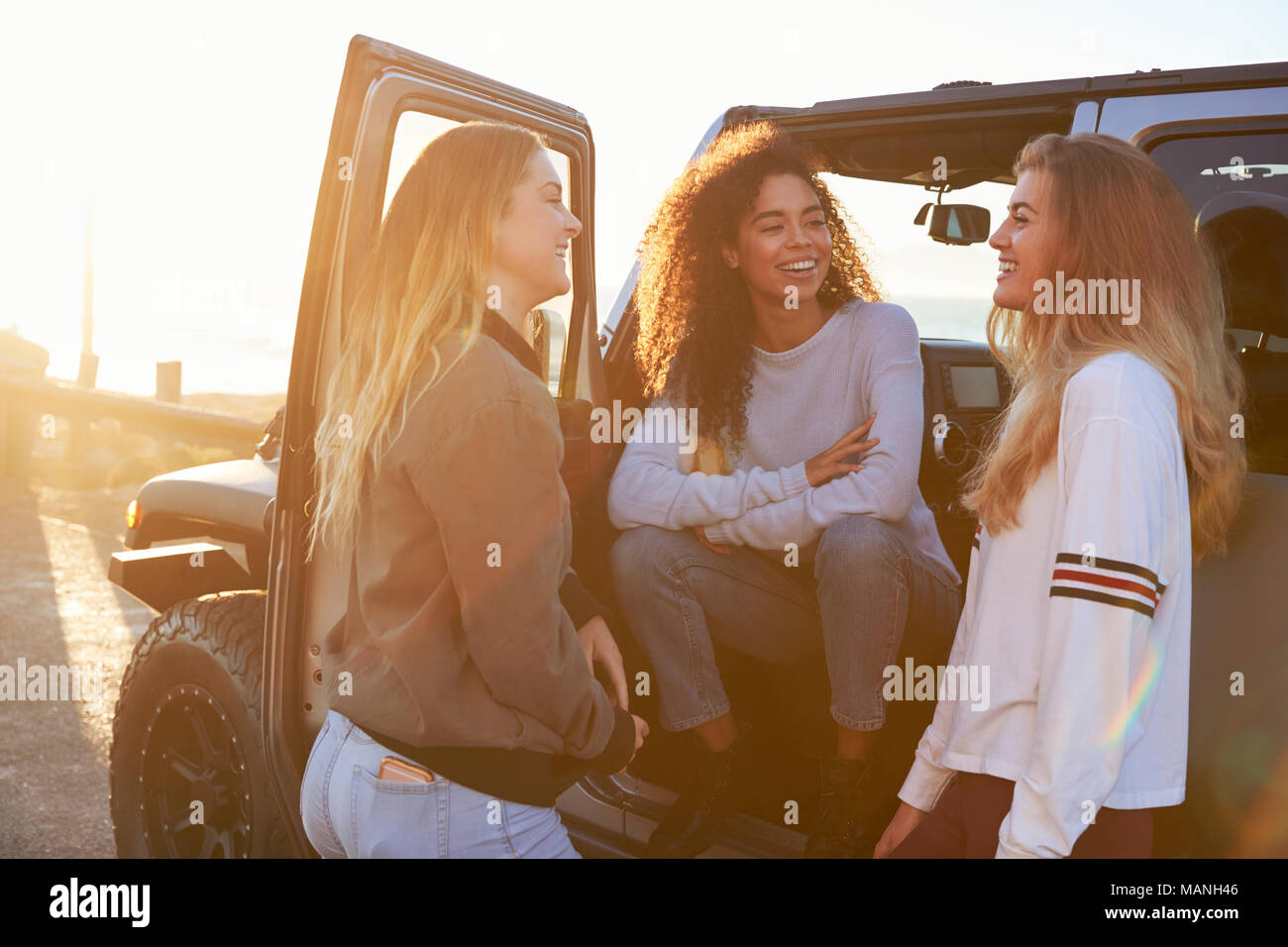 Three young female friends on a road trip talking beside car Stock Photo