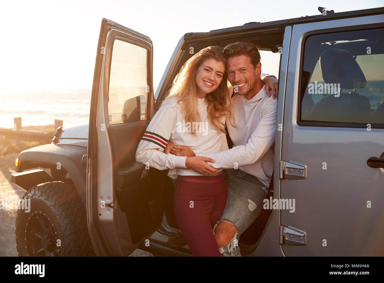 Young white couple on a road trip embracing by their car Stock Photo