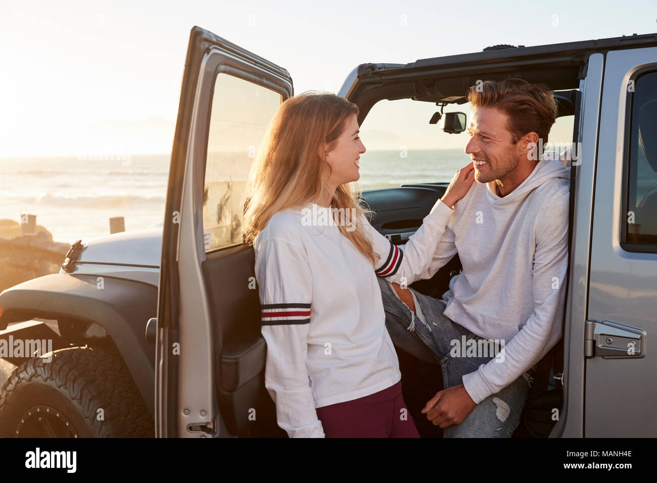 Young couple on road trip looking at each other by their car Stock Photo