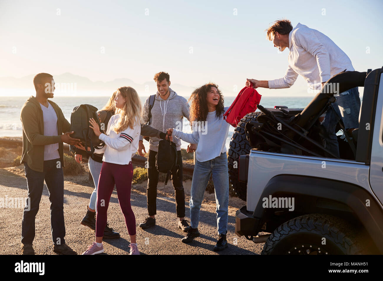 Young adult friends unloading backpacks from the back of car Stock Photo