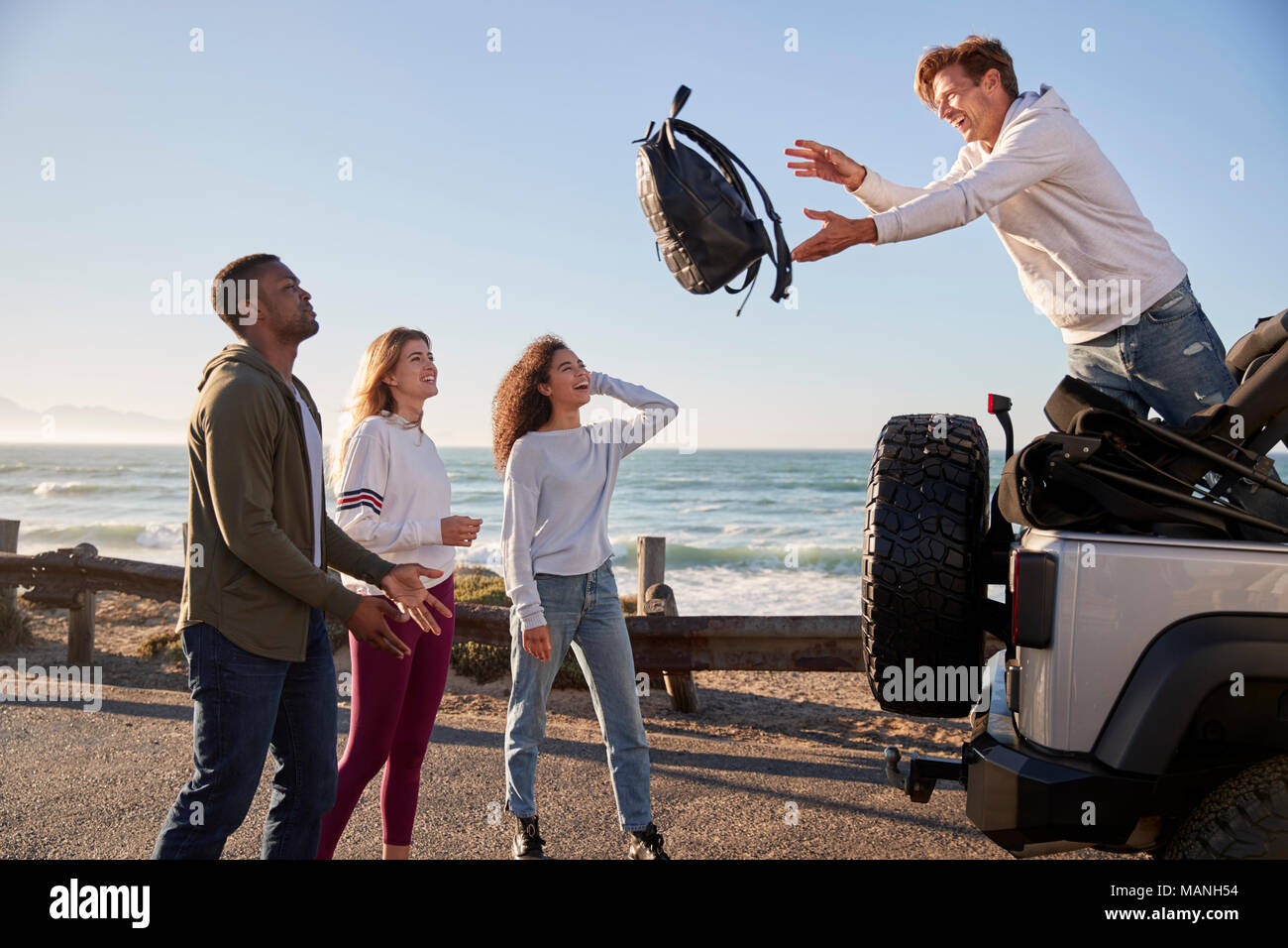 Four friends unloading backpacks from the back of their car Stock Photo