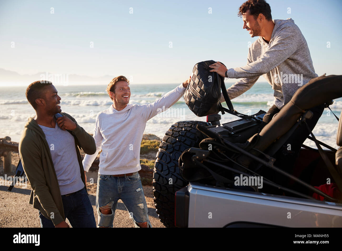 Three young adult male friends unloading backpacks from jeep Stock Photo