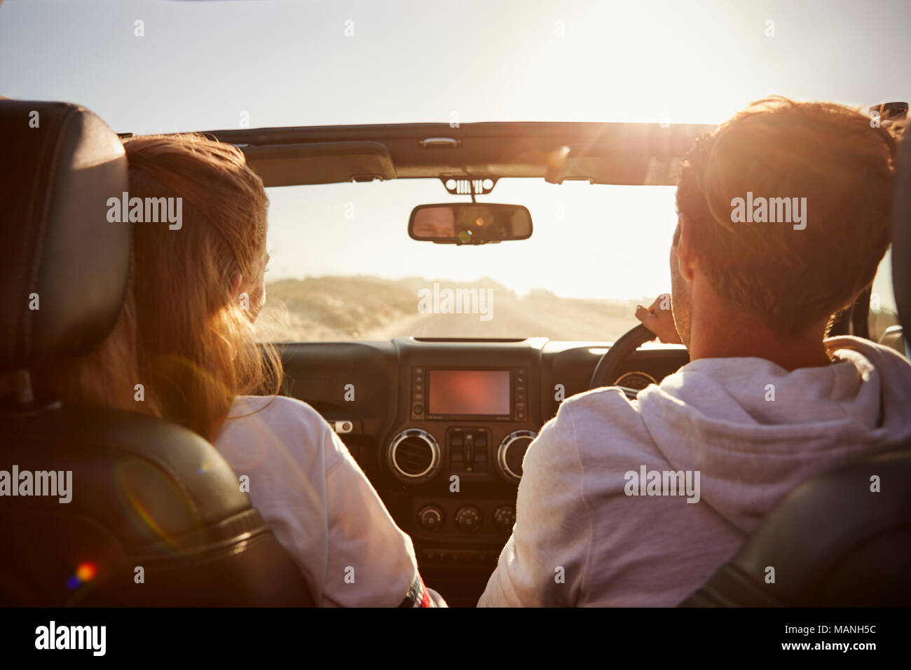 Young couple driving with sunroof open, rear passenger POV Stock Photo