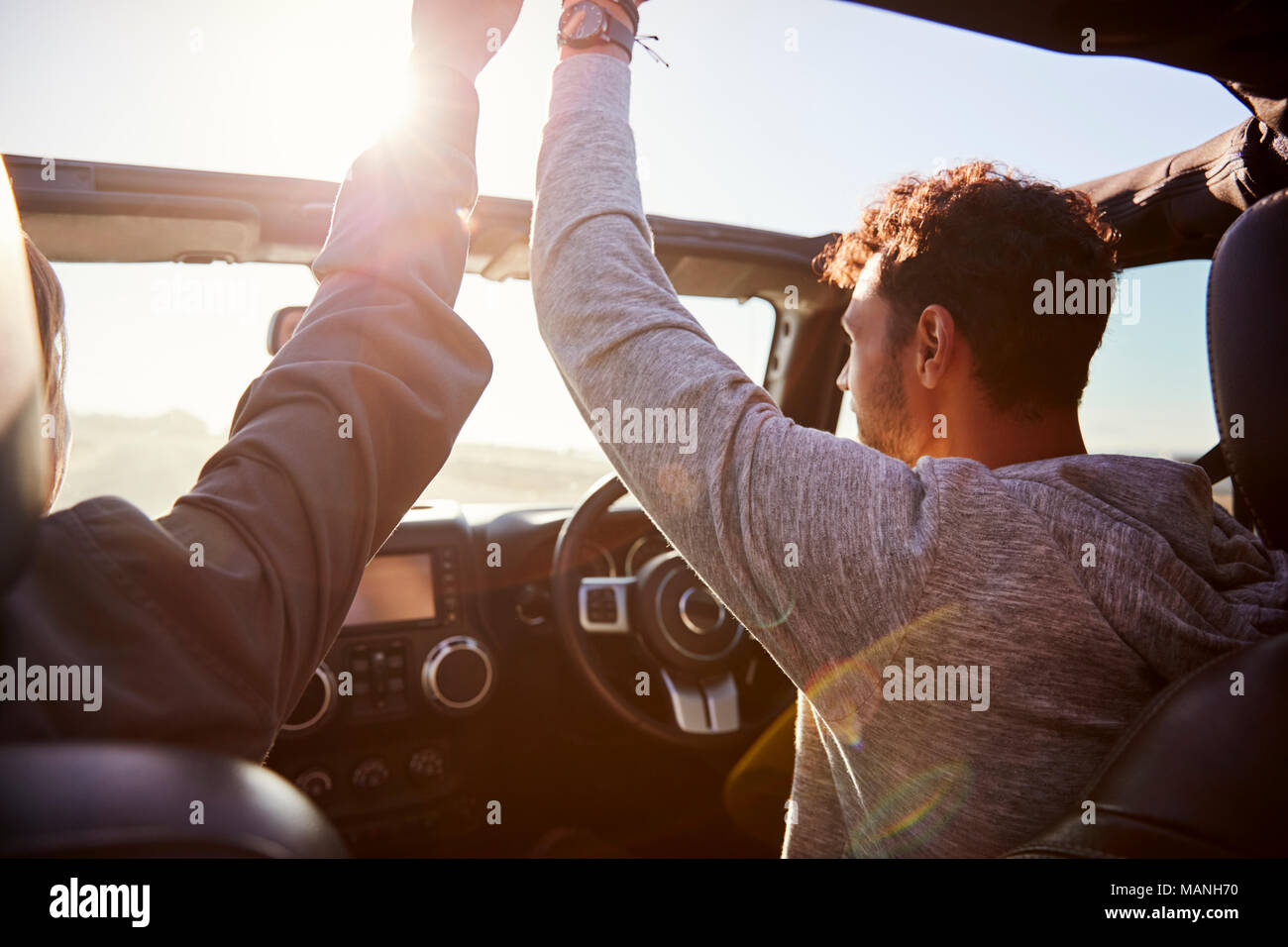 Young couple driving with sunroof open and hands in the air Stock Photo