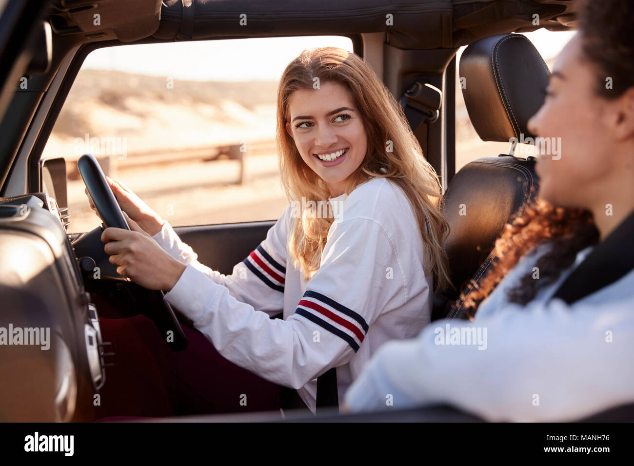 Two young female friends driving a car in the sun, side view Stock Photo