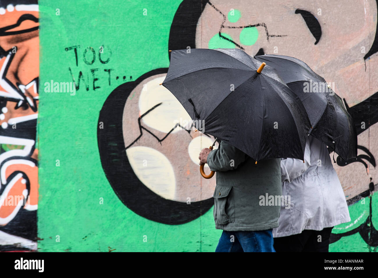 Too wet Bank Holiday weather in Southend on Sea, Essex, UK. Couple with umbrellas in the rain walking past graffiti wall with too wet, for literal use Stock Photo