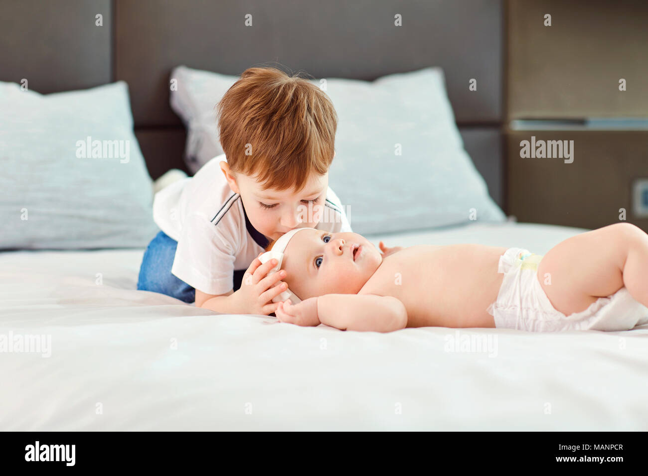 A little boy with his baby sister hugs and kisses on the bed. Stock Photo