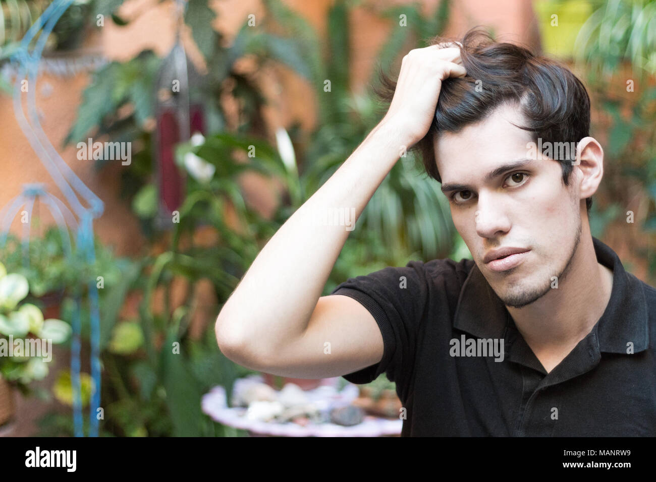 Portrait of a young man outdoors with his hand on his hair looking at camera, thinking and serious. Stock Photo