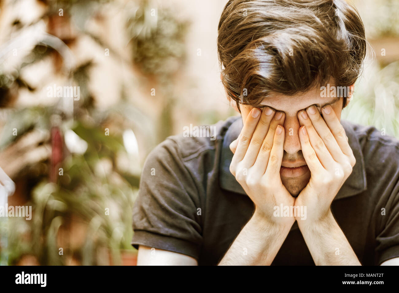 Young man sitting covering his eyes with his hands, sad and depressed concept. Stock Photo
