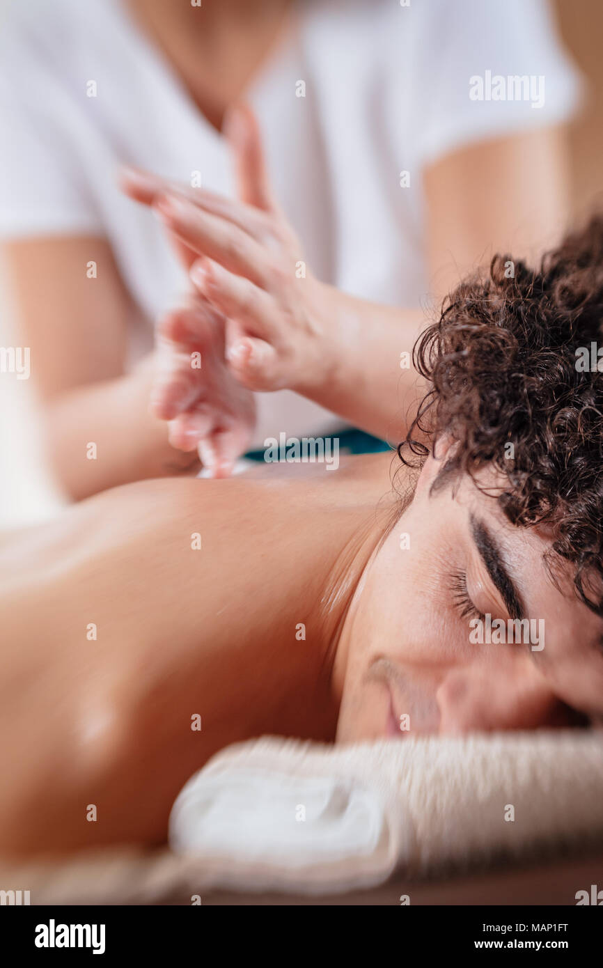 Close-up of handsome healthy young man enjoying relaxing back massage at beauty salon. Selective focus. Stock Photo