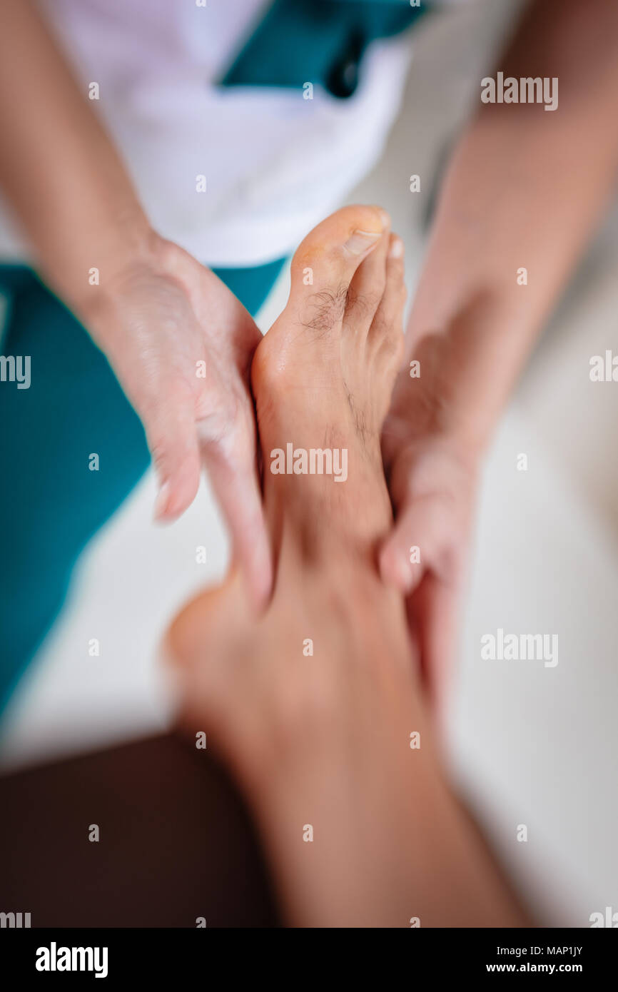 Close-up of a hads of female therapist massaging young man's foot at beauty salon. Selective focus. Stock Photo