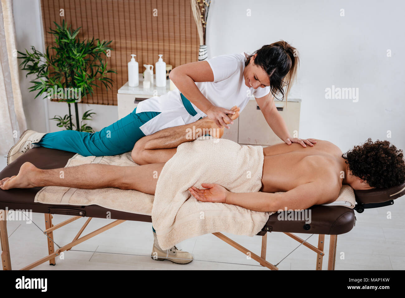 Handsome man lying down on massage table and getting healthy leg massage by young female therapist in the spa center. Stock Photo