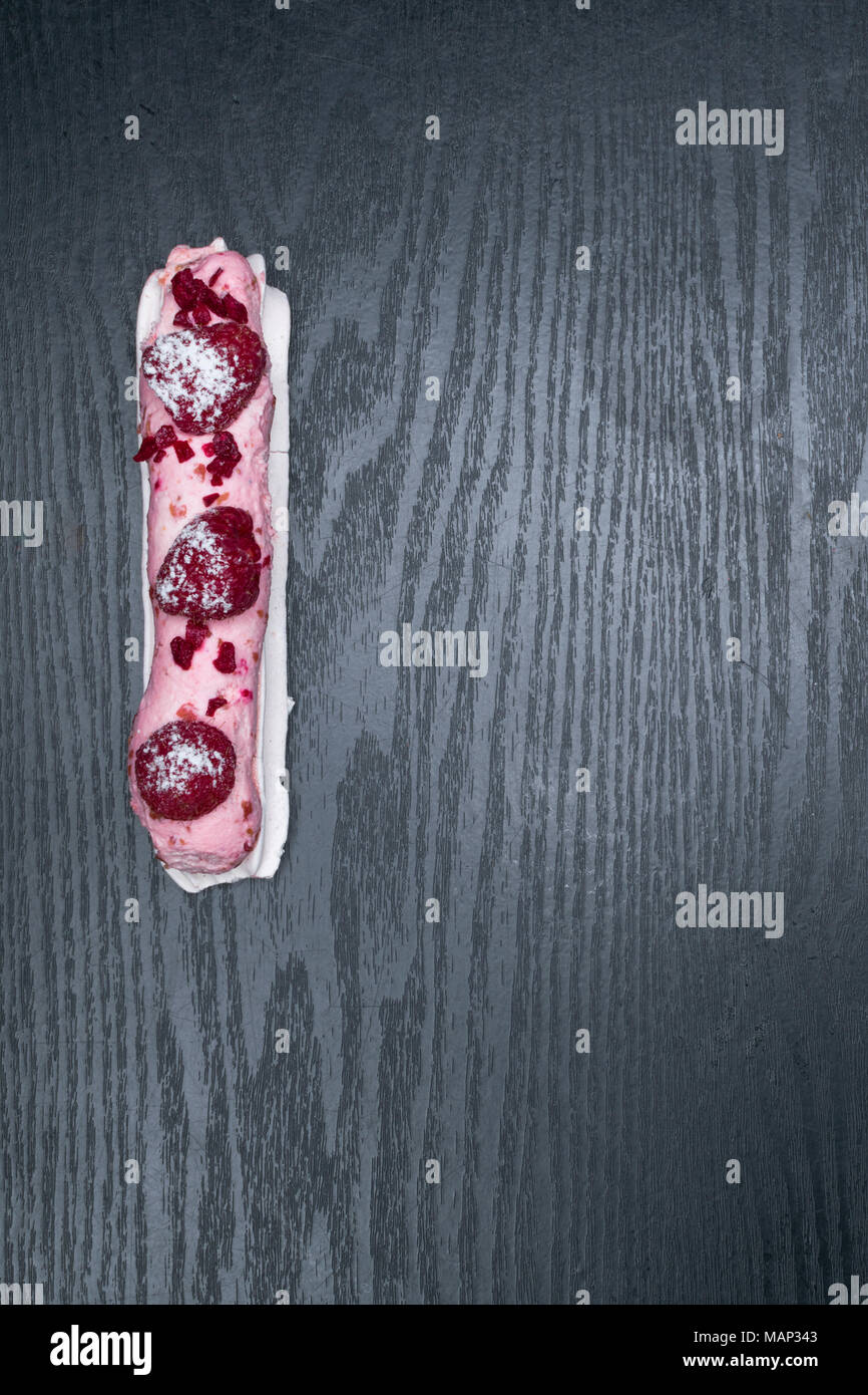 French traditional eclair, decorated with raspberry with cup of coffee on the dark wood table Stock Photo