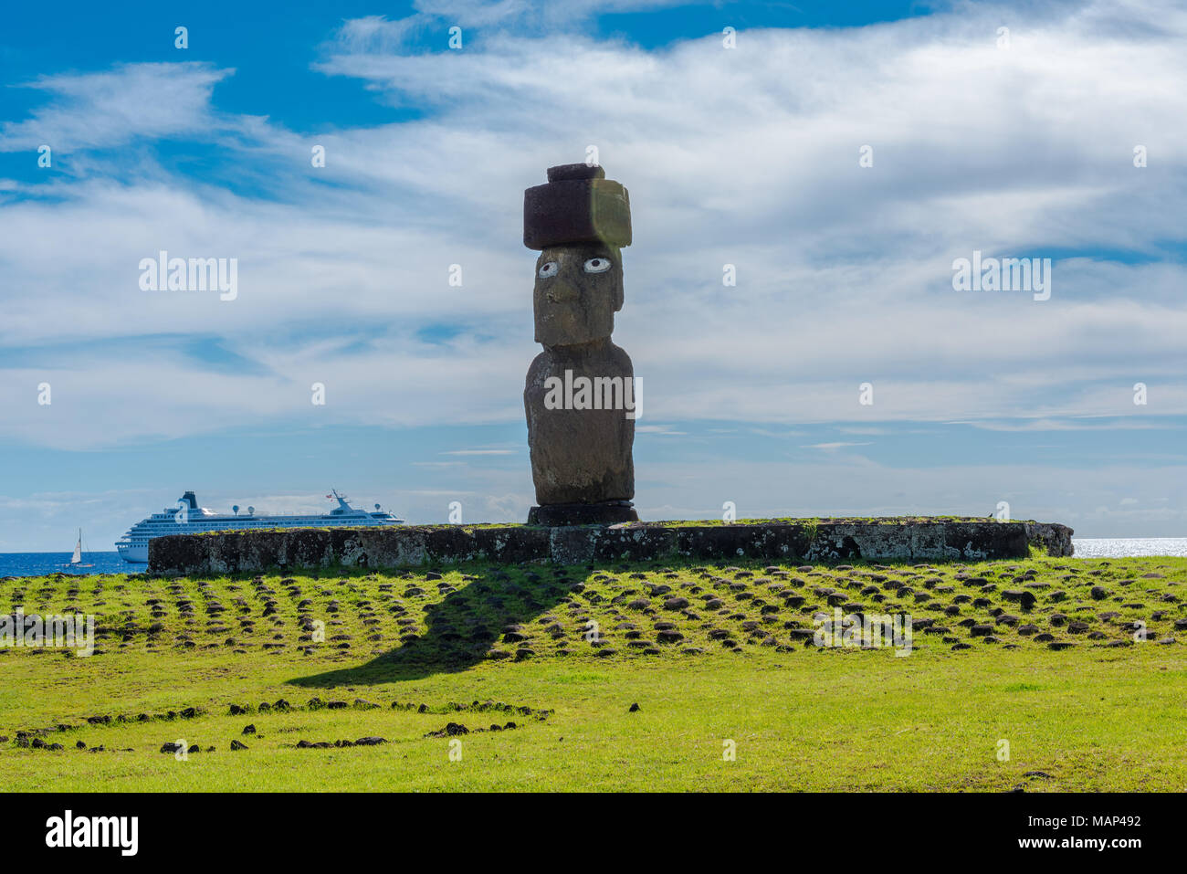 A large Moai statue with open eyes sits on top of an altar. A cruise ship is in the background. Editorial Use Only. Stock Photo