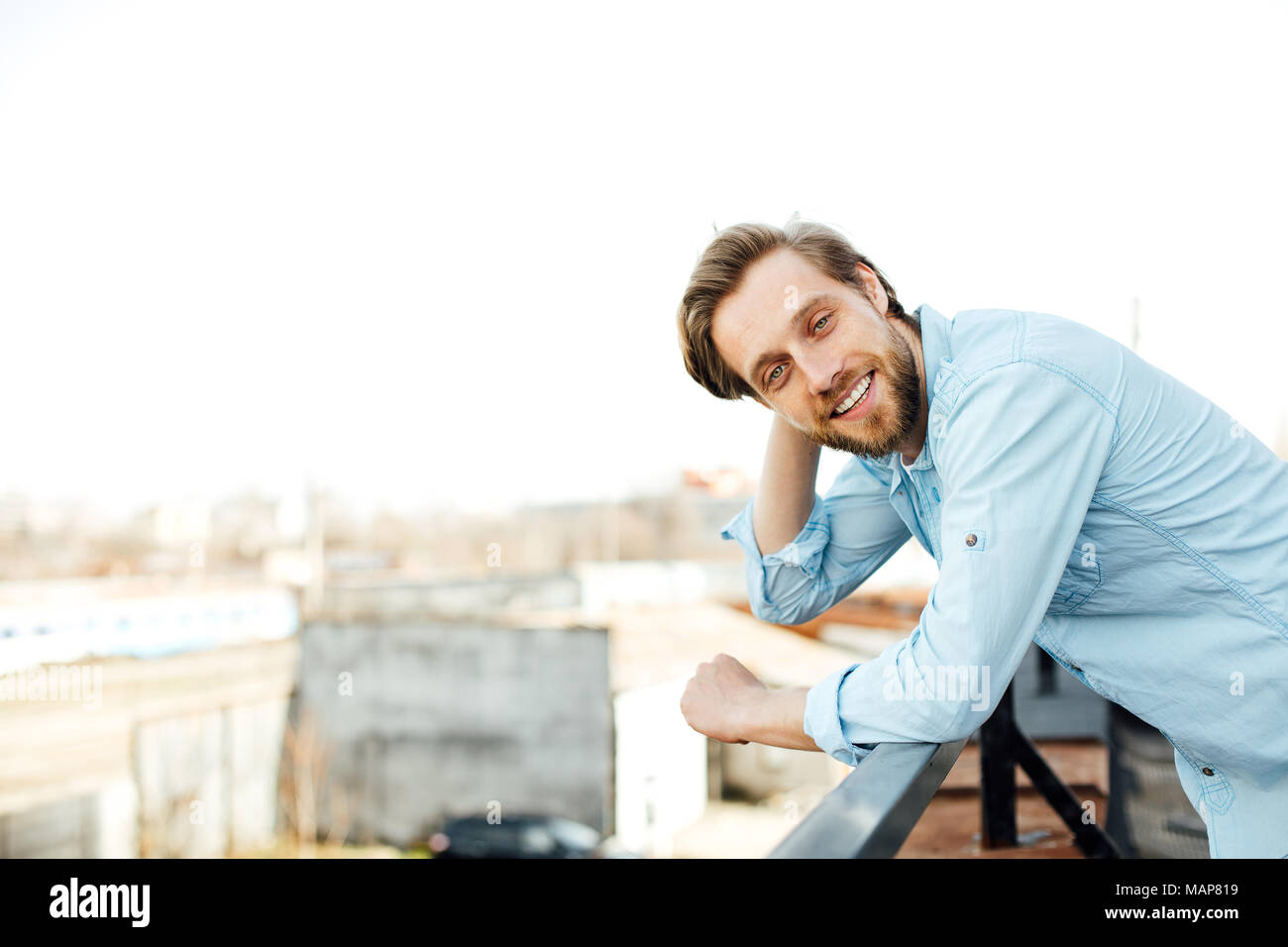 casual handsome blonde man standing outside in blue shirt, smiling and having a positive attitude, looking to camera Stock Photo