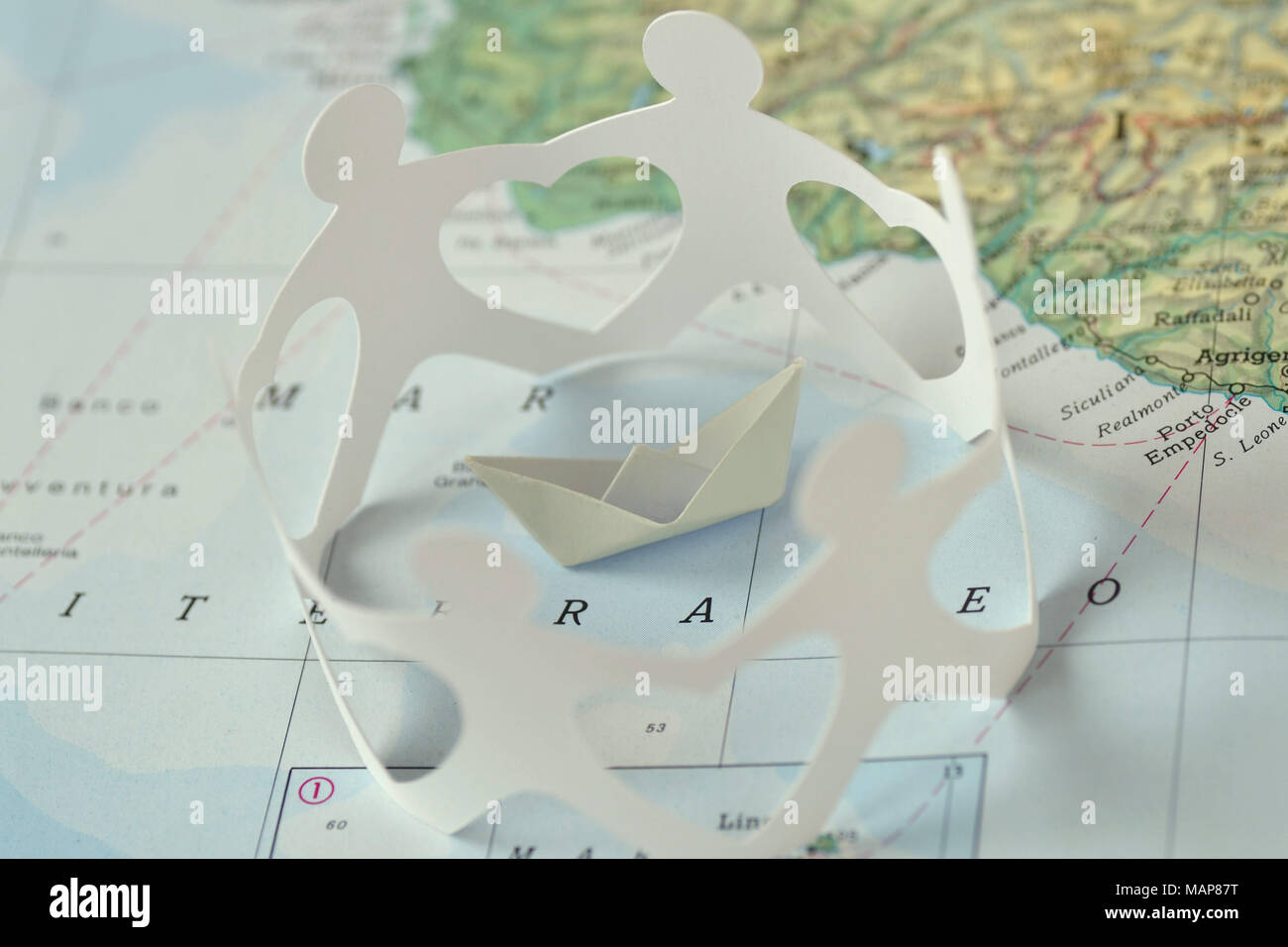 Paper boat and paper people in a circle holding hands on a map - Immigration and solidarity concept Stock Photo