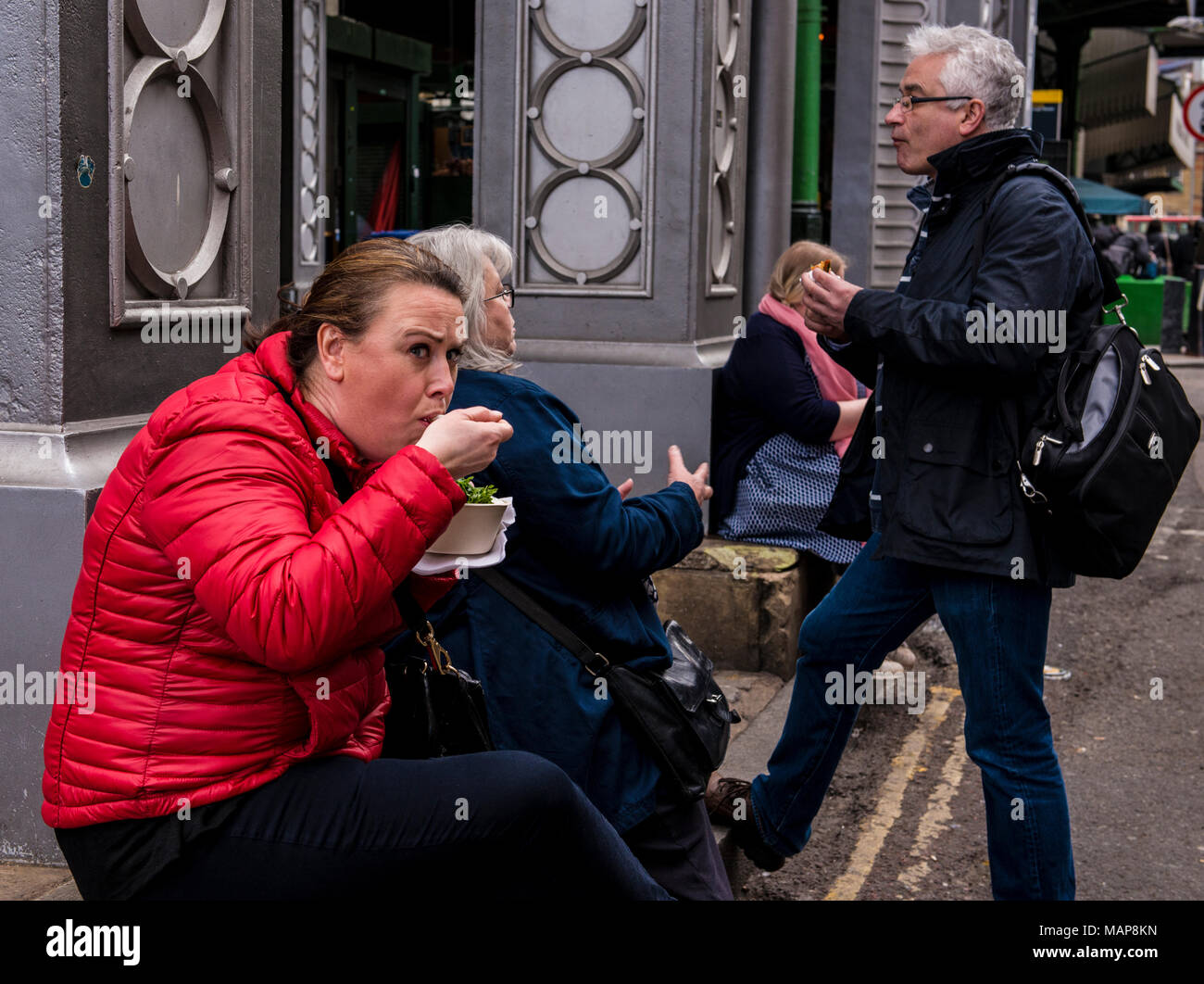 Woman in red coat eating street food near Borough Market, Southwark, London, England, UK Stock Photo