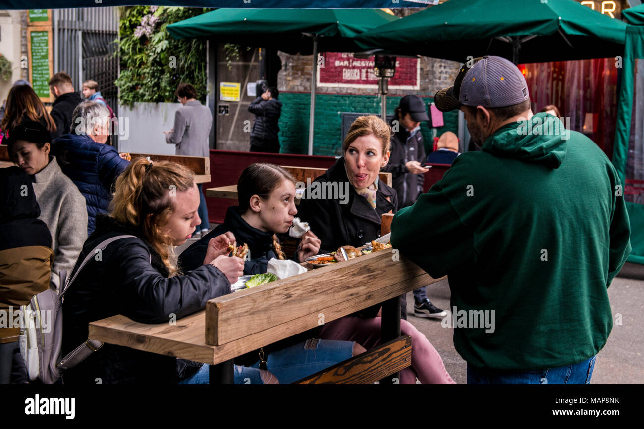 Family eating food at wooden bench, Borough Market, London, England, UK Stock Photo