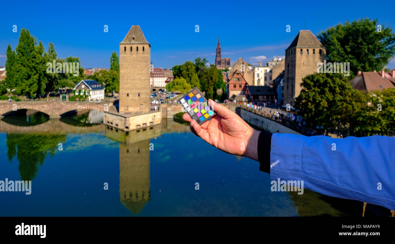 Hand holding out a Macbeth mini color checker with Ponts Couverts, covered bridges and skyline in the distance, Strasbourg, Alsace, France, Europe, Stock Photo