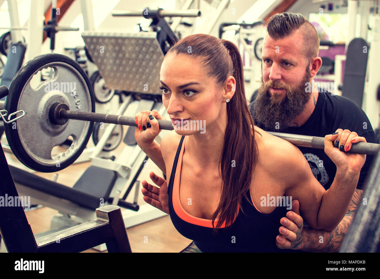 Bearded coach helps a woman in a gym with dumbbells. Stock Photo