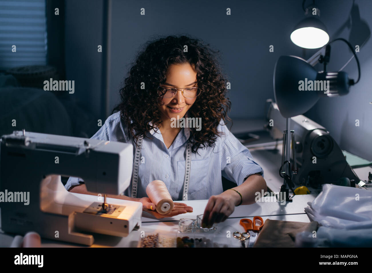 dressmaker is threading beads in front of stitching machine in black