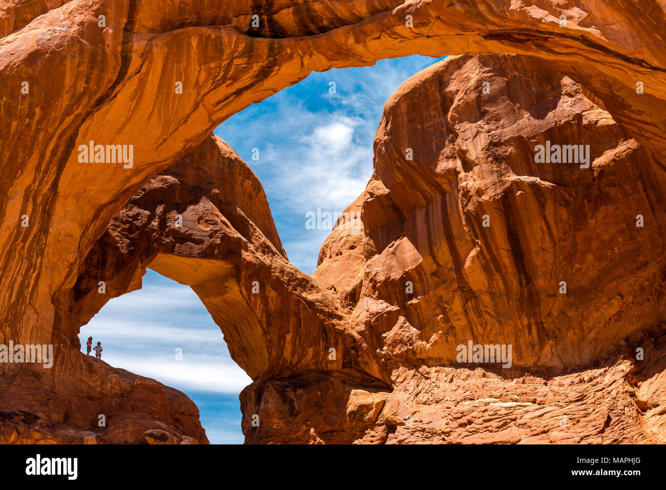 The silhouette of two adventurers after a hike under Double Arch inside Arches national park near Moab, Utah state, USA. Stock Photo