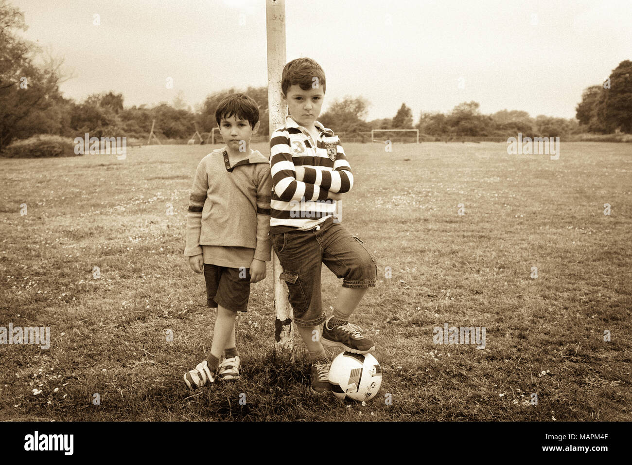 Two young boys with football leaning on goalpost in park Stock Photo