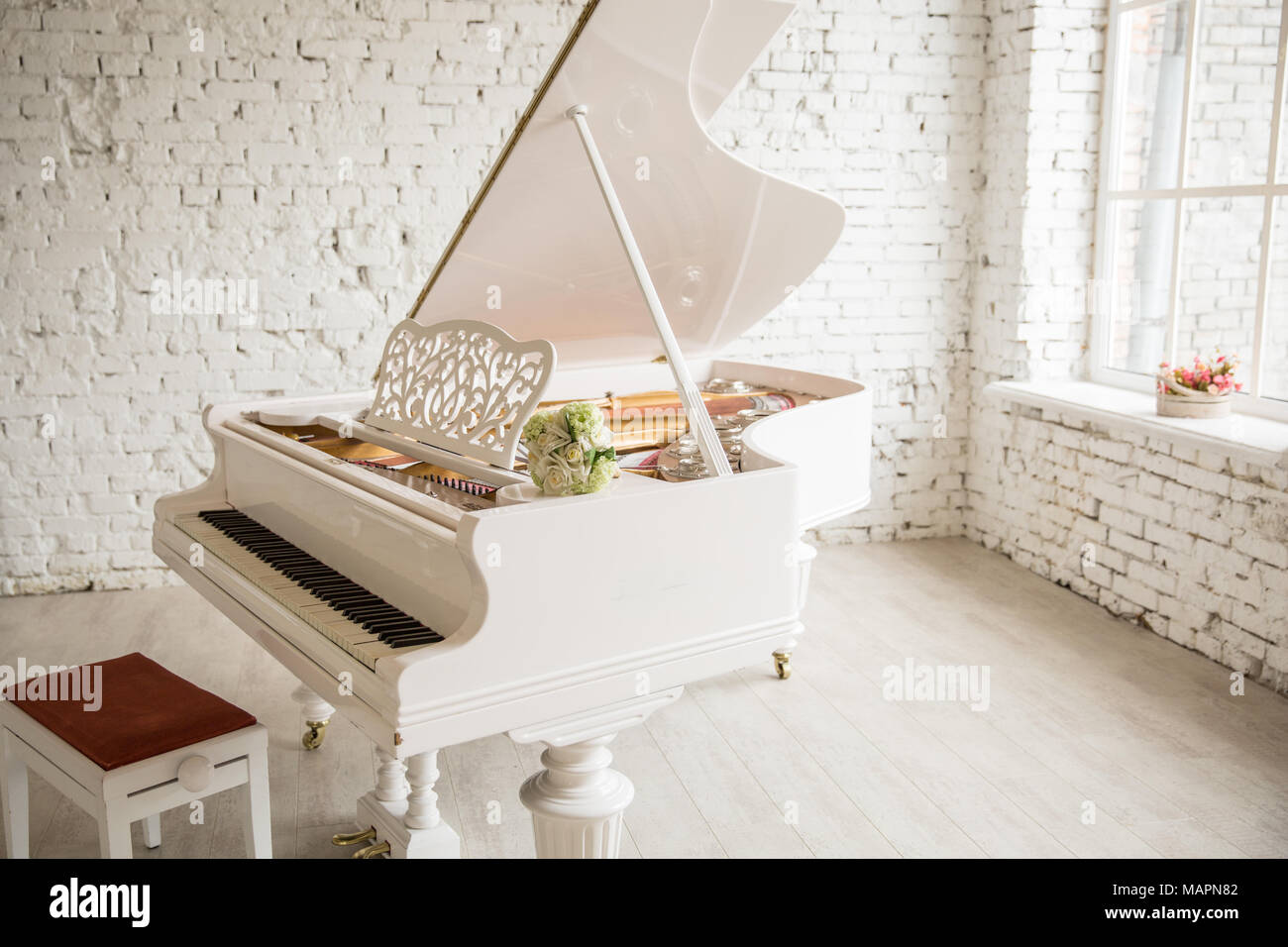 white grand piano standing in elegant white interior of Brick walls