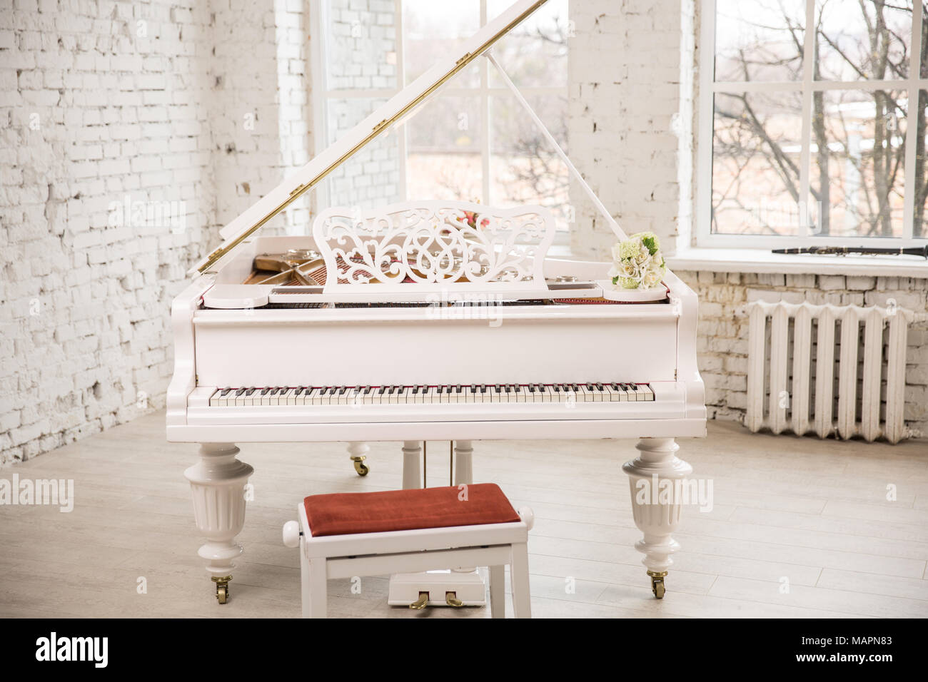 white grand piano standing in elegant white interior of Brick walls