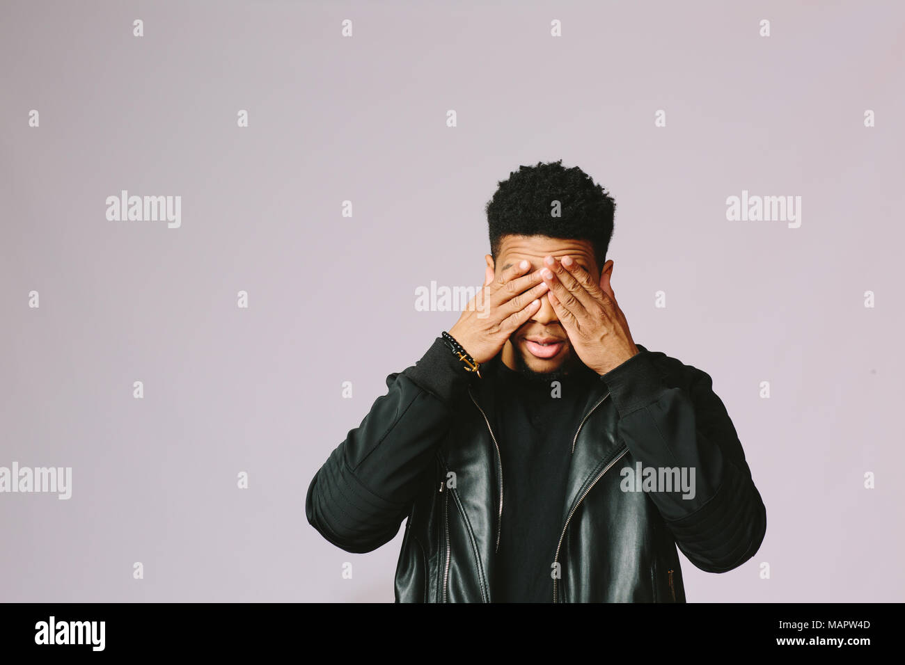 Portrait of a cool young man covering his eyes with both hands, isolated on studio background Stock Photo