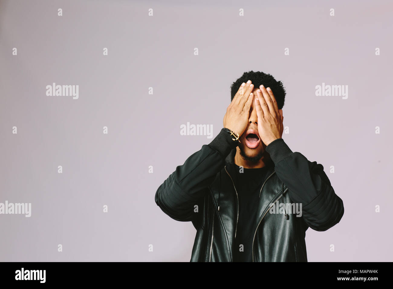 Portrait of a young man covering his eyes with both hands, isolated on ...