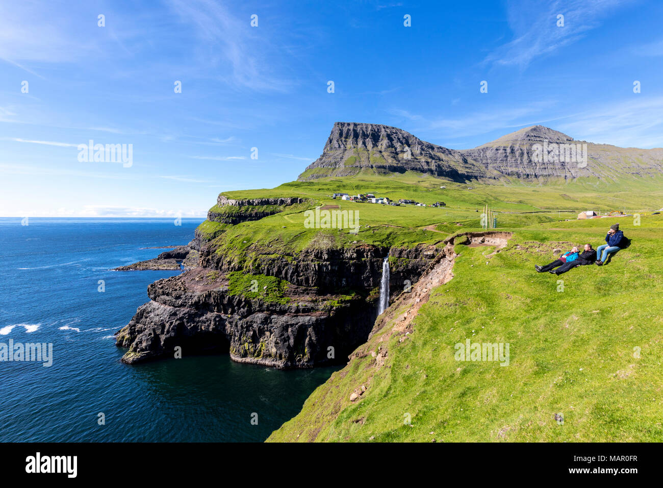 People admire the ocean from green meadows on cliffs, Gasadalur, Vagar Island, Faroe Islands, Denmark, Europe Stock Photo