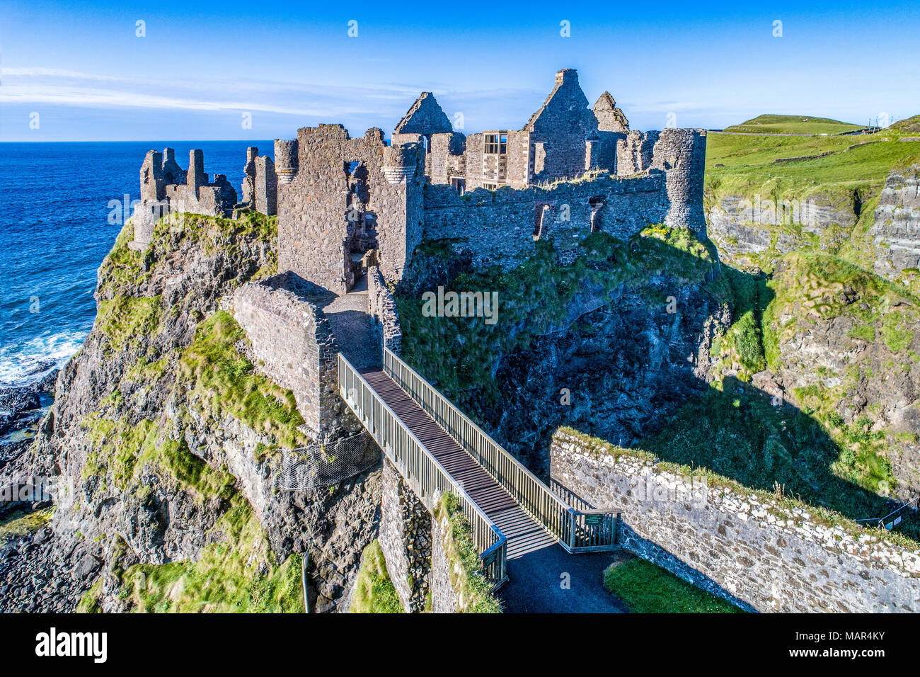 Ruins of medieval Dunluce Castle on a steep cliff. Northern coast of County Antrim, Northern Ireland, UK. Aerial view at sunset light. Stock Photo