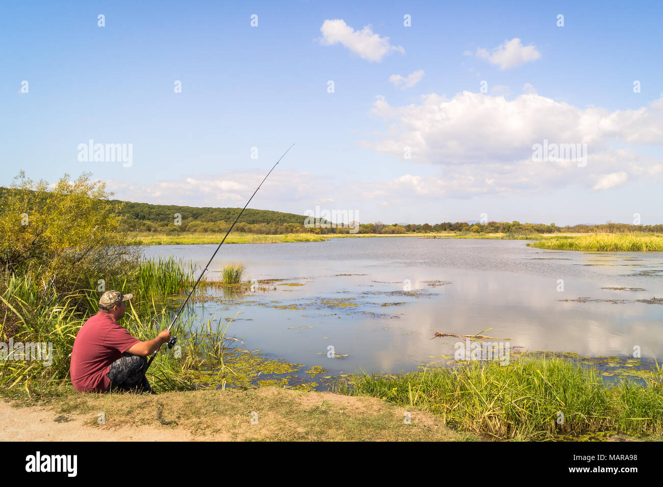 Fisherman on the shore of the lake. Fishing adventure against the backdrop of the scenic landscape of Lake Khanka in the far east of Russia Stock Photo