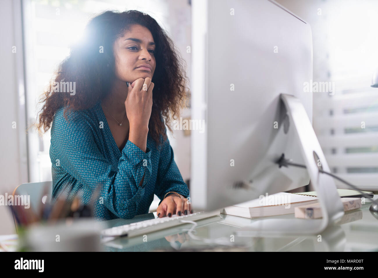 Beautiful young black woman sitting at her desk in front Stock Photo