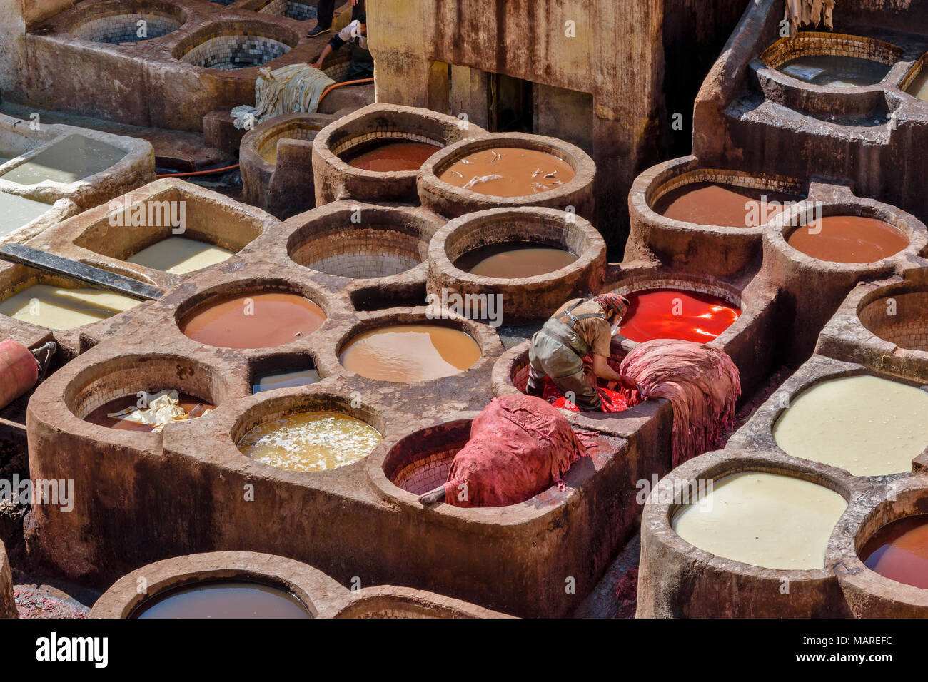 MOROCCO FES MEDINA SOUK CHOUWARA TANNERIES VATS WITH COLOURED DYES AND HIDES WORKER WITH RED DYE AND SKINS Stock Photo