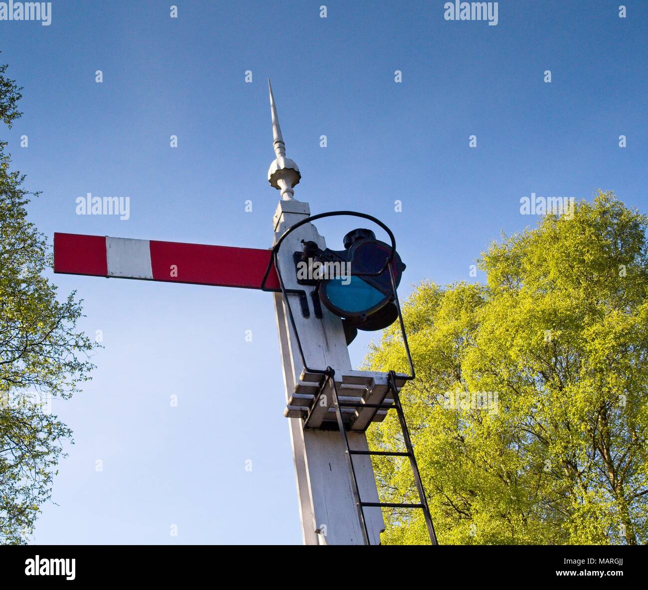 A closeup view of a vintage railway signal in the stop position, against a blue sky. Stock Photo