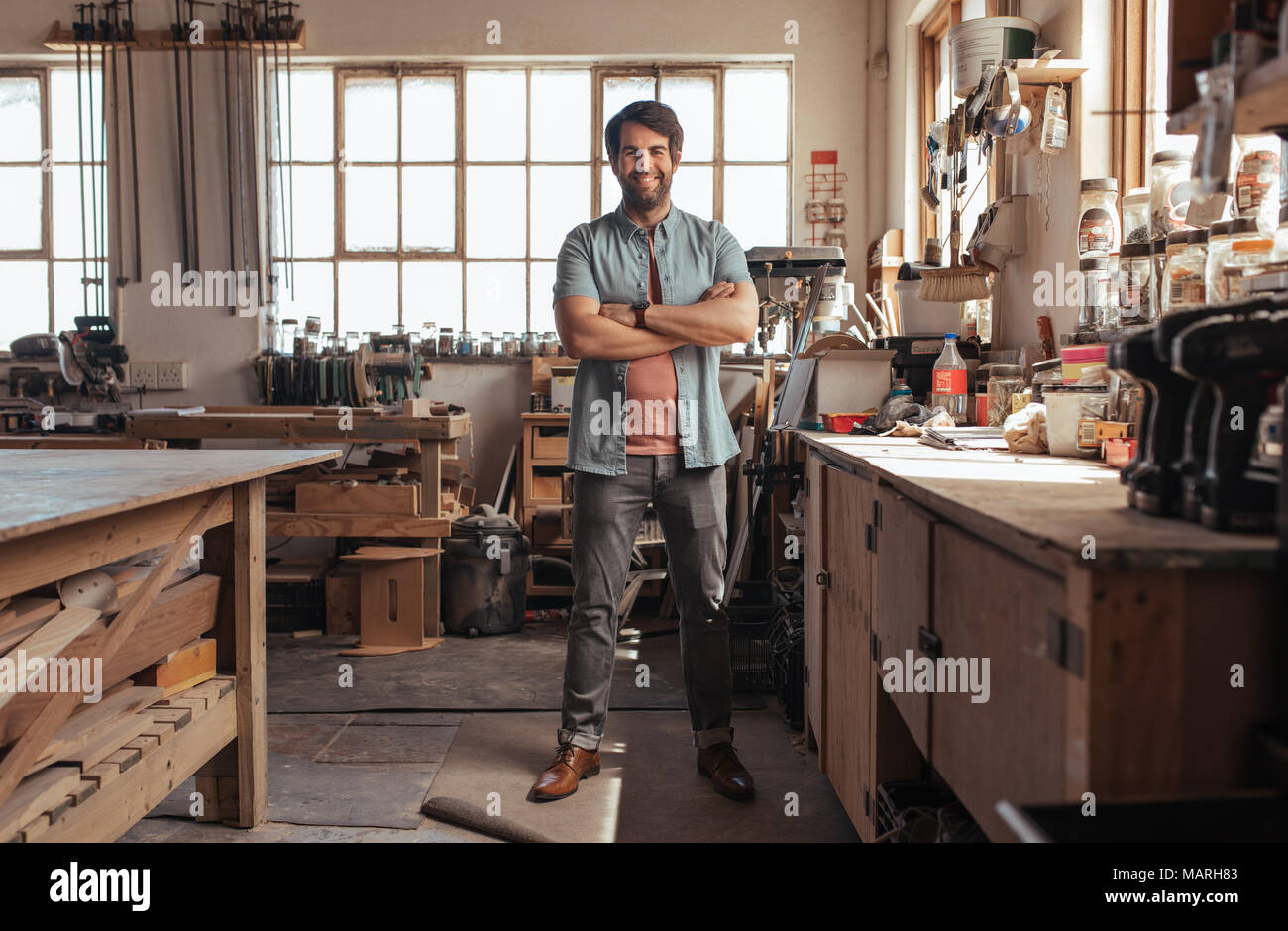 Smiling young woodworker standing in his workshop full of 
