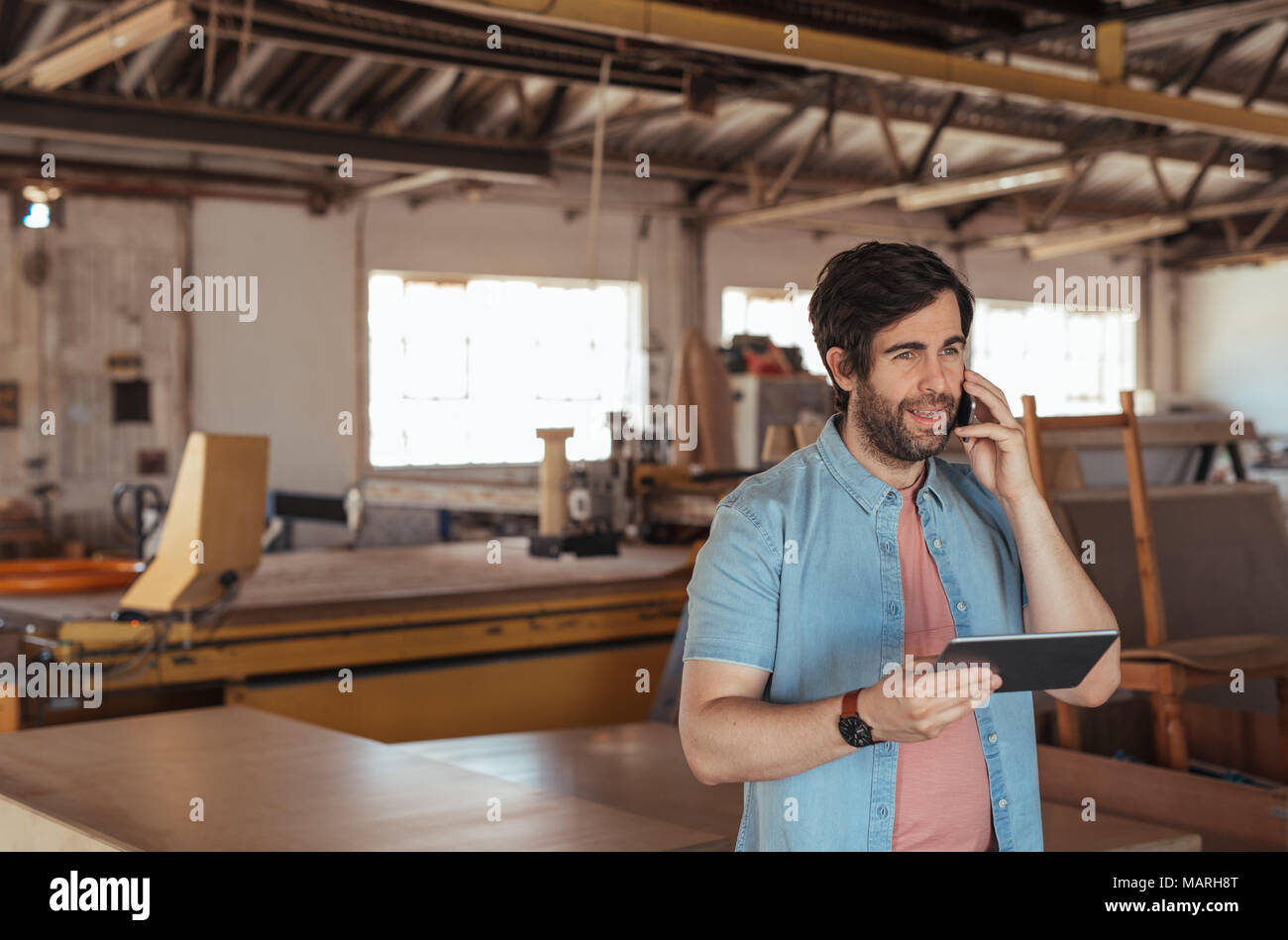 Woodworker using a cellphone and tablet in his workshop Stock Photo