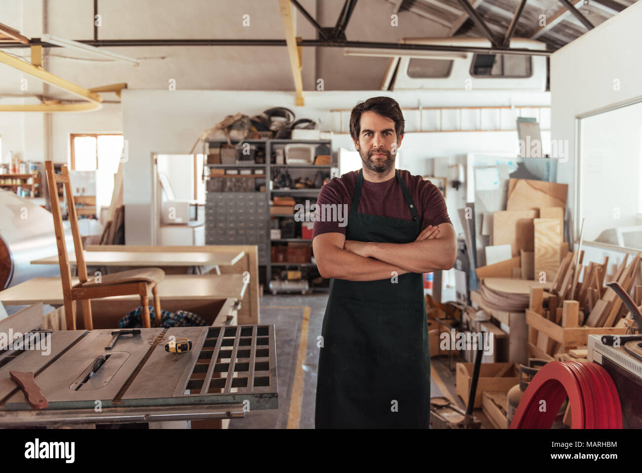 Craftsman standing by a bench saw in his woodworking shop Stock Photo