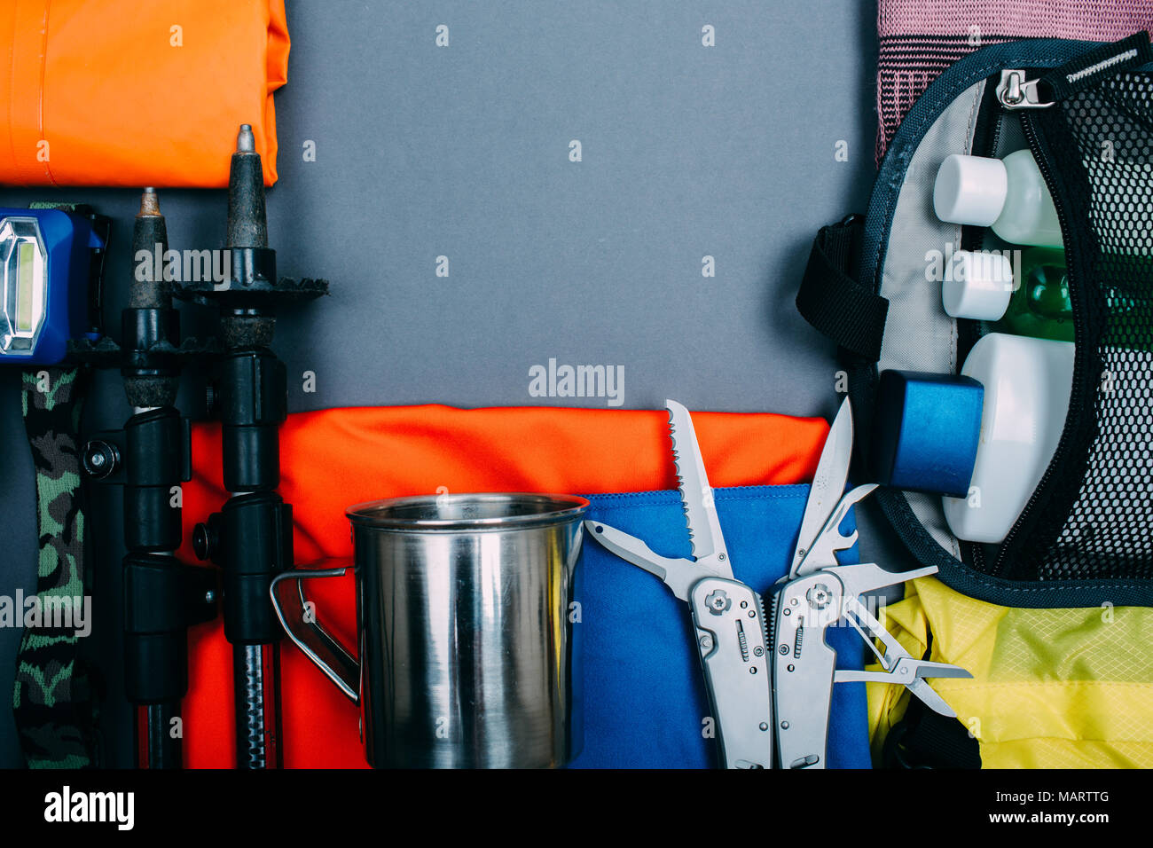 Top view of equipment for hiking and travel on gray background with empty space in the middle. Items include trekking pole, multi tool, towel, hygiene Stock Photo